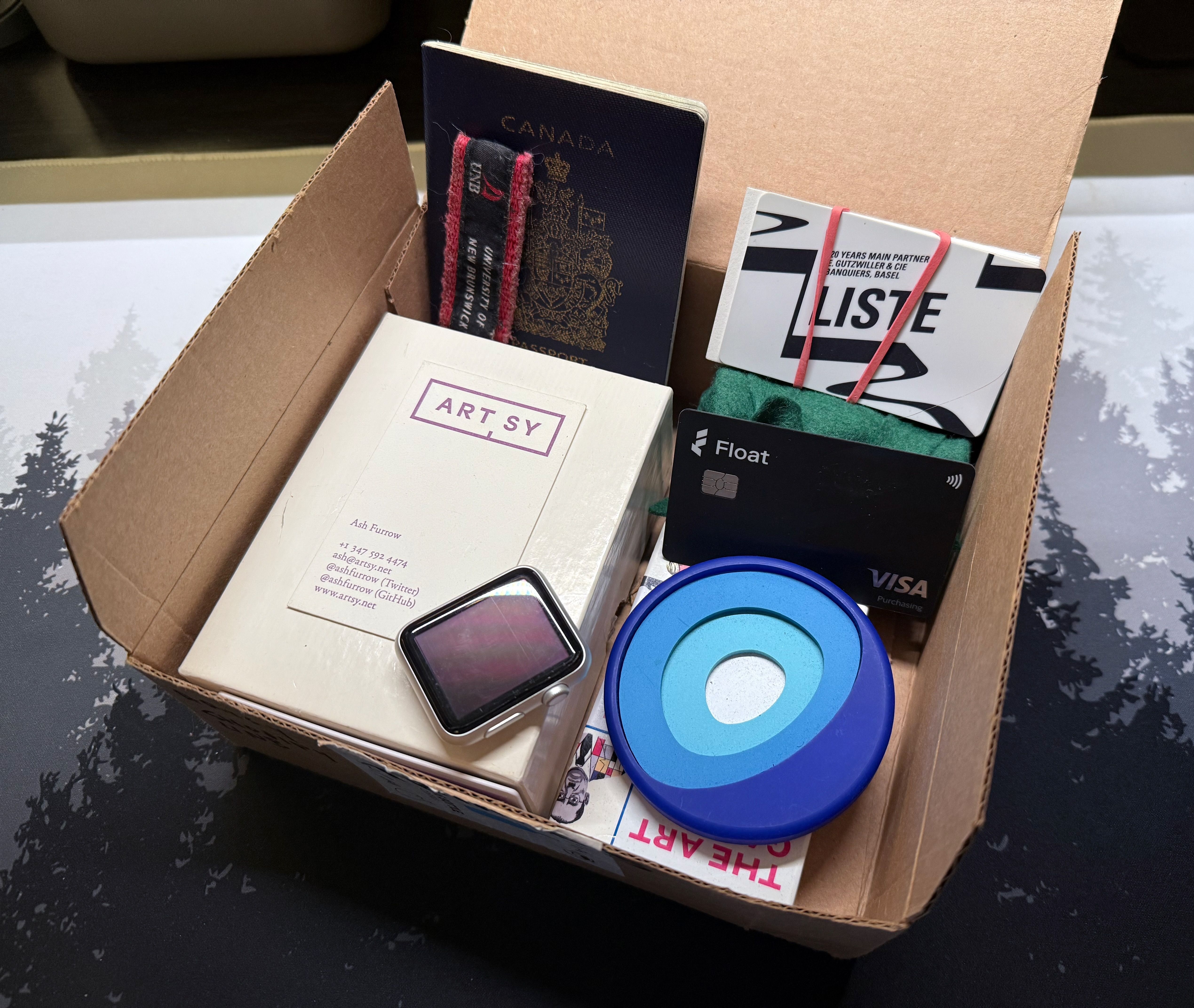 A box with old Artsy business cards, a UNB keychain, a Series 0 Apple Watch, an old passport, and other items.